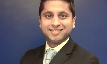 Smiling man in a suit against a blue background.
