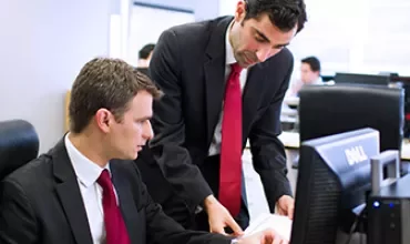 Two businessmen in suits working at a computer in an office.