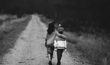 Two children walking on a rural path, one with an arm around the other, in black and white.