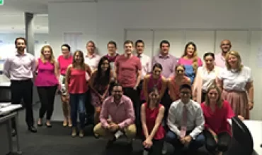 A group of people standing in an office, wearing pink colors.