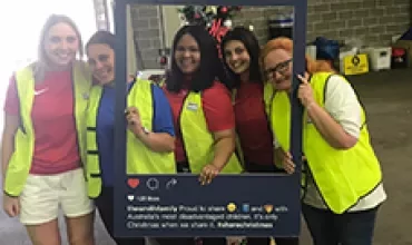 Group of four women wearing high-vis vests, smiling and holding a #sharechristmas frame.