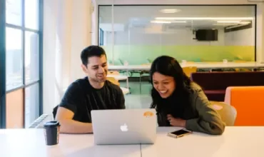 Two people smiling while looking at a laptop in a modern office.