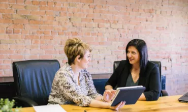 Two women discussing work at a conference table with a tablet.