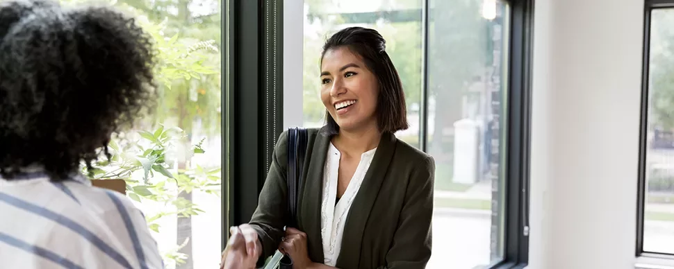 Smiling woman in business attire shaking hands near a window.