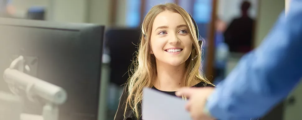 Smiling woman at her desk in an office setting, receiving a document.