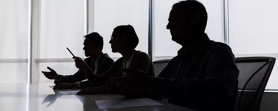 Silhouettes of three people sitting at a table during a discussion.