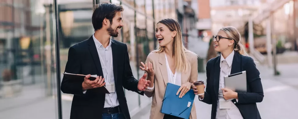 Three professionals walking and talking outside near office buildings.