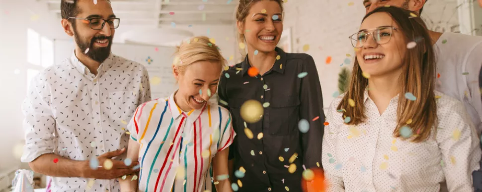 Group of people smiling and laughing with colorful confetti falling around them.