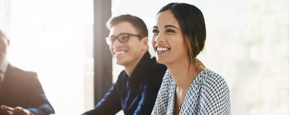 Two people smiling and sitting at a table in an office setting.