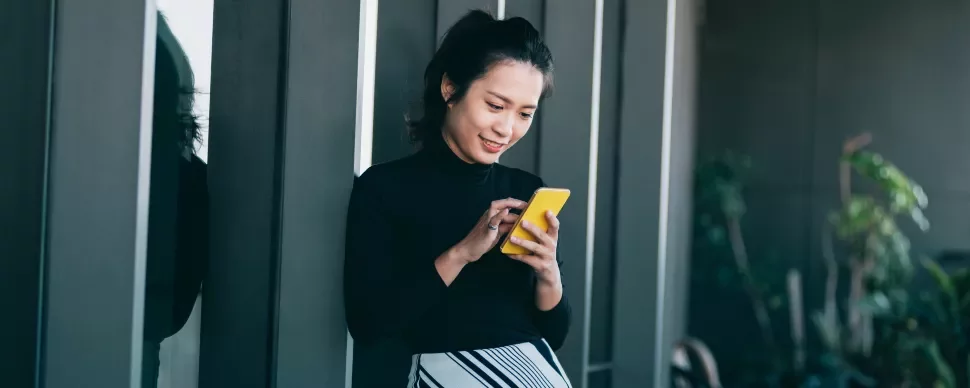 Woman smiling while using a yellow smartphone outside a building.