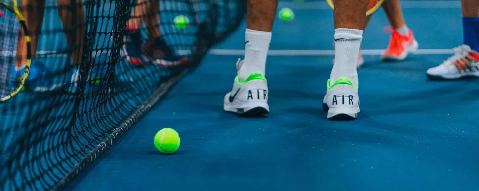 Tennis players on a blue court with tennis balls scattered around.