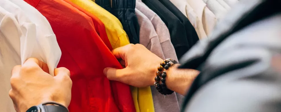 Person browsing colorful shirts on a clothing rack.