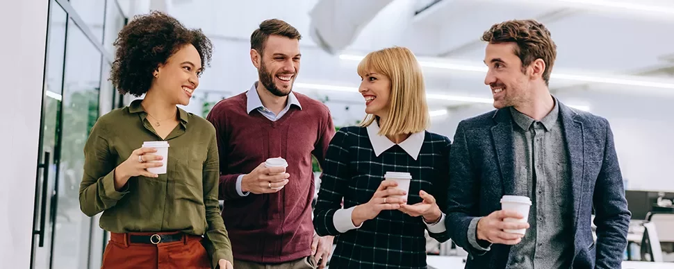 Four colleagues walking and holding coffee cups while smiling.