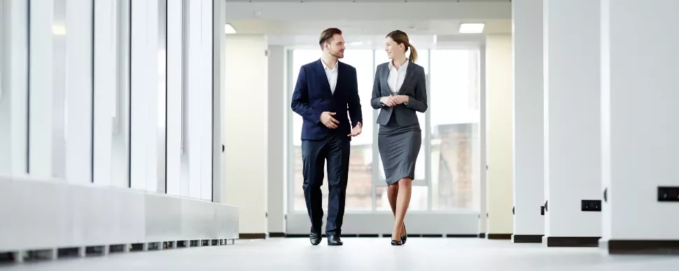 Two business professionals walking and talking in an office corridor.