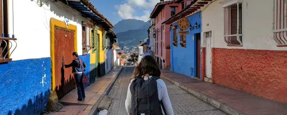 Person walking down a colorful street with mountains in the background.