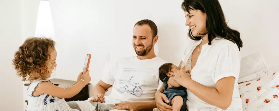 A family sits together on a bed; the girl uses a smartphone.