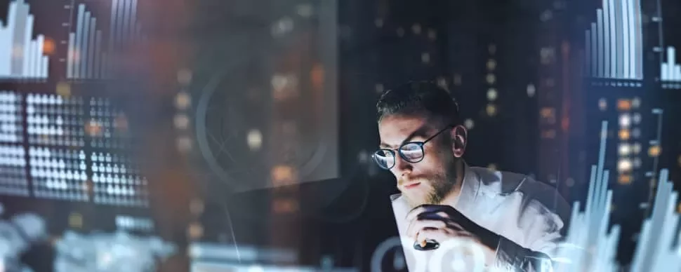 Man working on laptop, analyzing data on screen in dark room with graphs.
