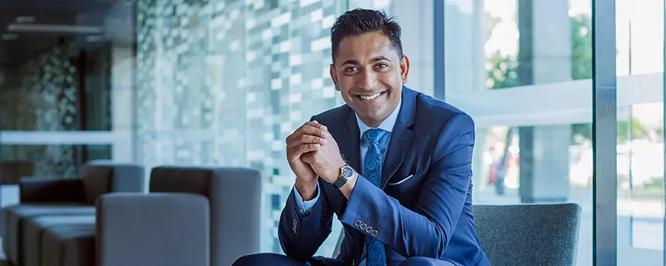 Smiling man in a blue suit sitting in a modern office setting.