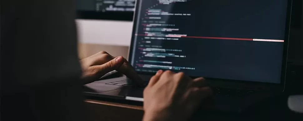 Person typing code on a laptop in a dimly lit room.