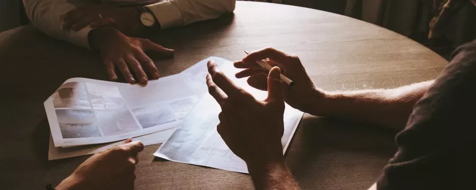 People discussing papers around a wooden table.