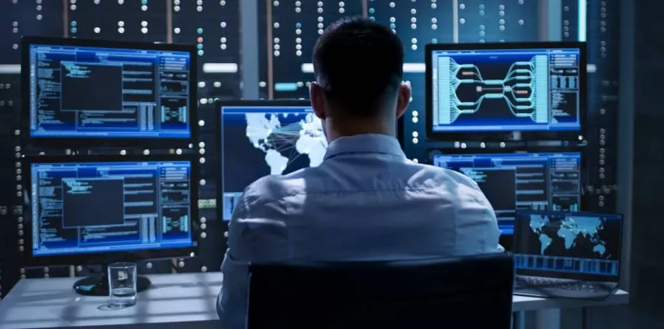 Person working at a desk with multiple computer monitors displaying data and maps.