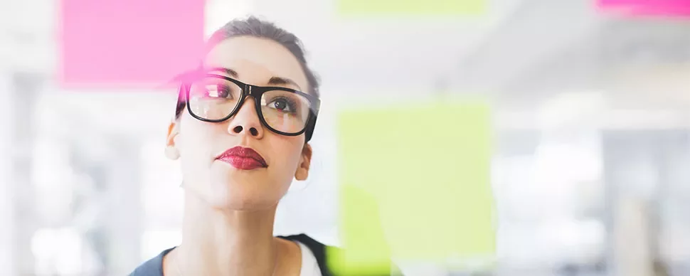 Person with glasses looking at colorful sticky notes on glass.
