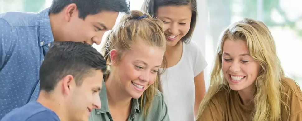 Group of smiling young people looking at a laptop together.