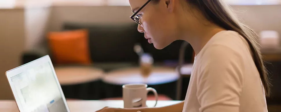 Person with glasses focused on a laptop in a cozy cafe.