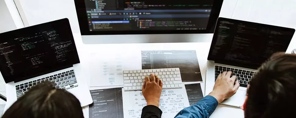 Three people collaborate on laptops with code on screens at a desk.