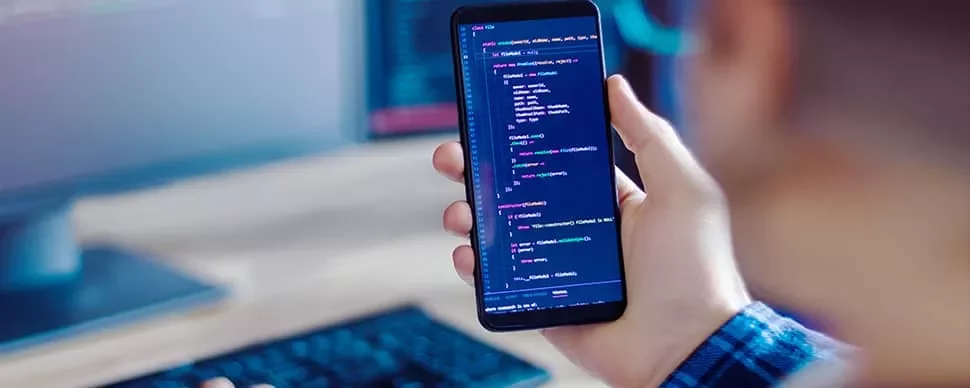 Person holding a smartphone displaying code, with a computer keyboard in the background.