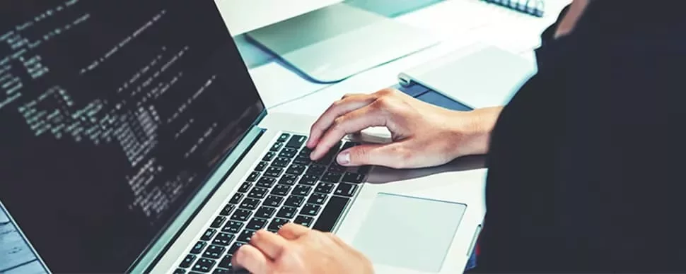 Person typing on a laptop with code displayed on the screen.