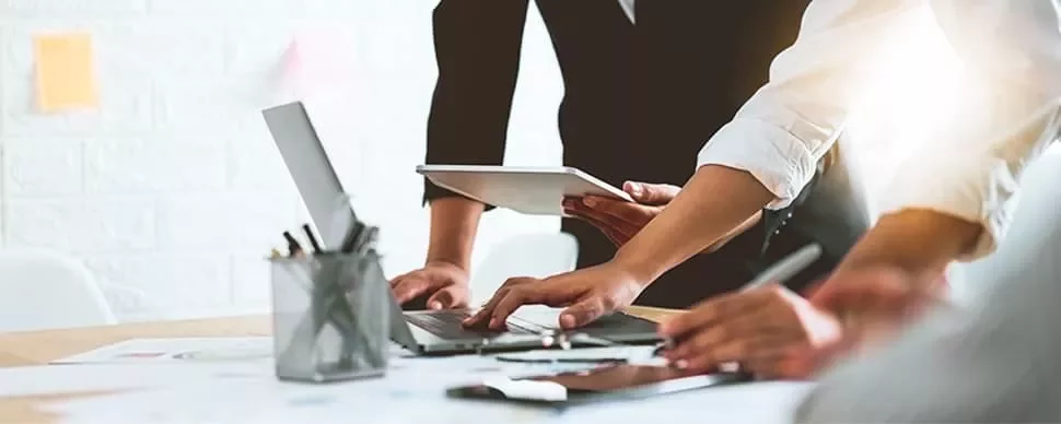 Group of people working together on laptops and tablets at a desk.