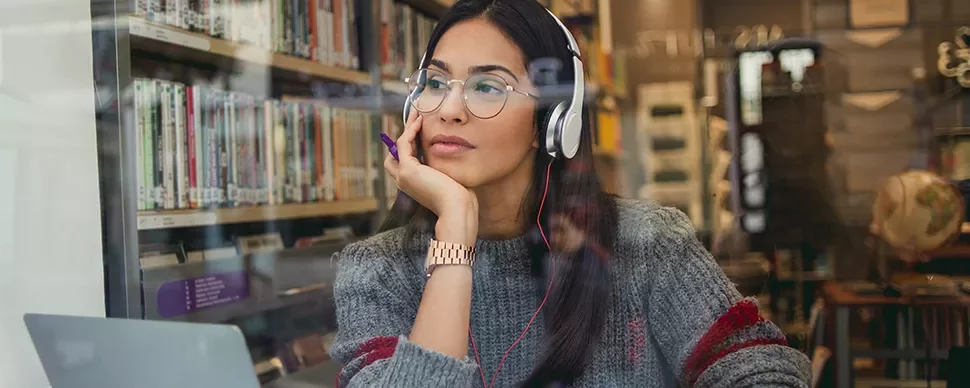 Woman wearing headphones looking out a library window, with books in the background.