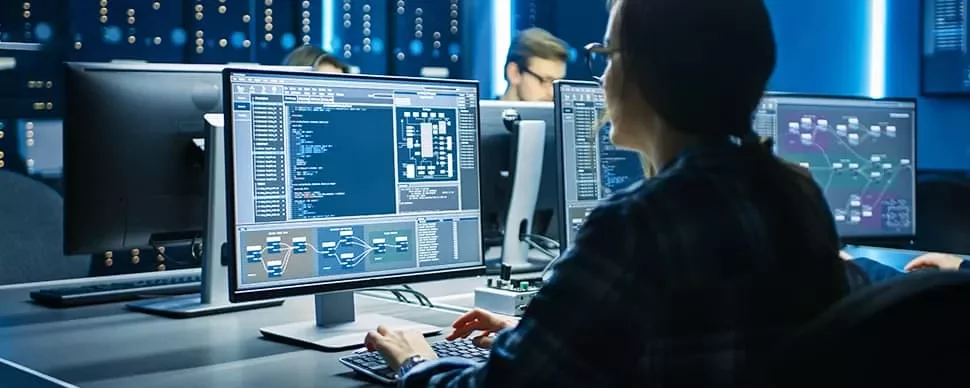 Person working on multiple computer screens in a dark office.