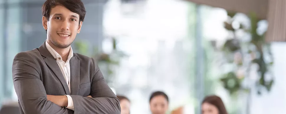 Confident businessman with arms crossed, standing in a bright office.