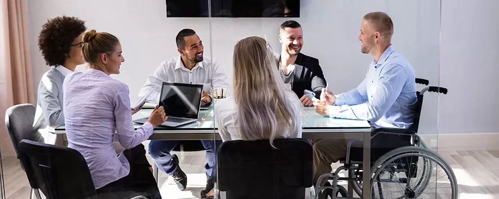 A diverse group of colleagues smiling in a meeting around a glass table.