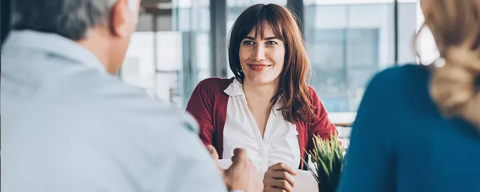 Woman smiling in a meeting with two people in an office setting.