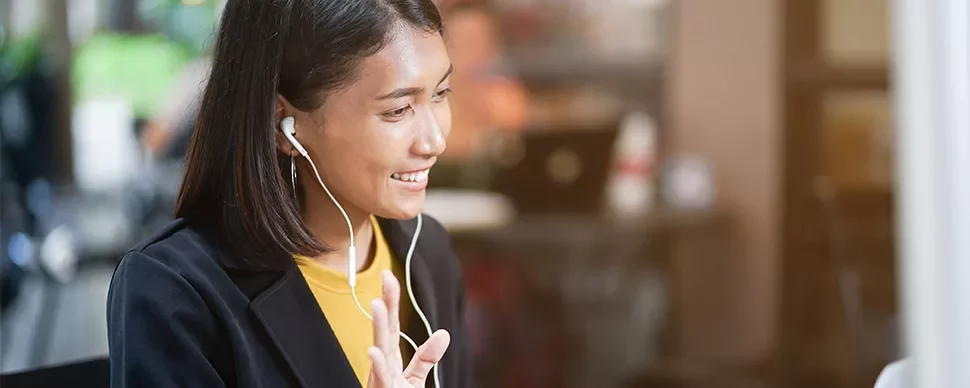 Woman wearing earbuds, smiling in a cafe during a video call.