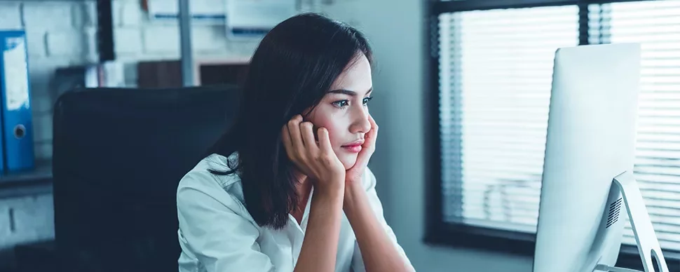 Woman sitting at a desk, looking at a computer screen with focus.