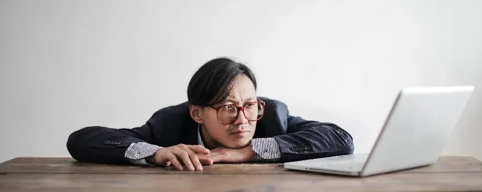 Man with glasses looking at a laptop on a wooden table.