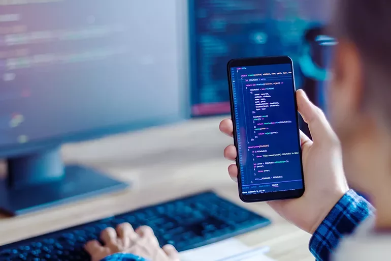 Person holding a smartphone with code visible on the screen.