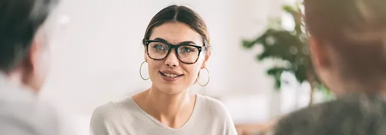 Woman with glasses and hoop earrings talking to two people.