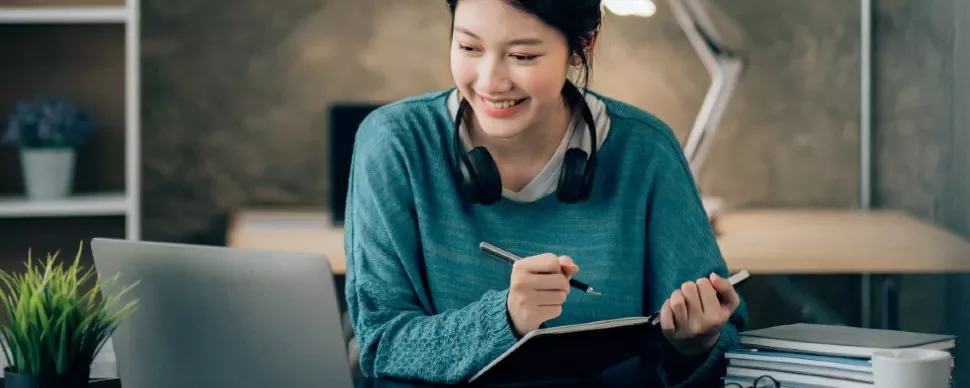 Woman smiling while writing in a notebook at her desk