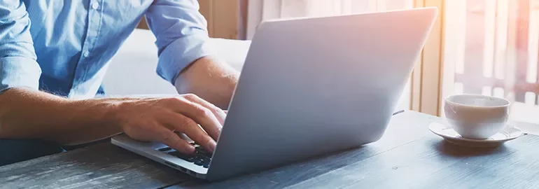 Person typing on a laptop at a wooden table with a cup of coffee.