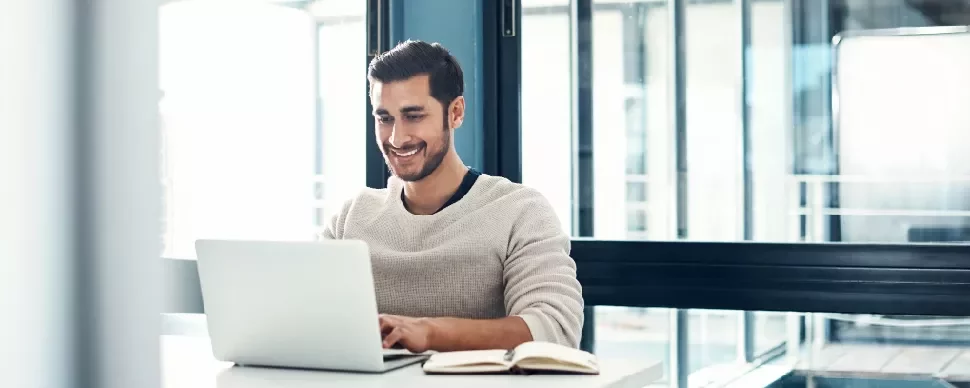 Man smiling while working on a laptop at a desk.
