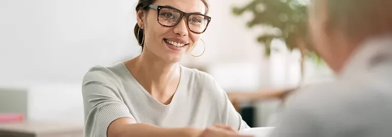 Smiling woman with glasses sitting at a table during a conversation.