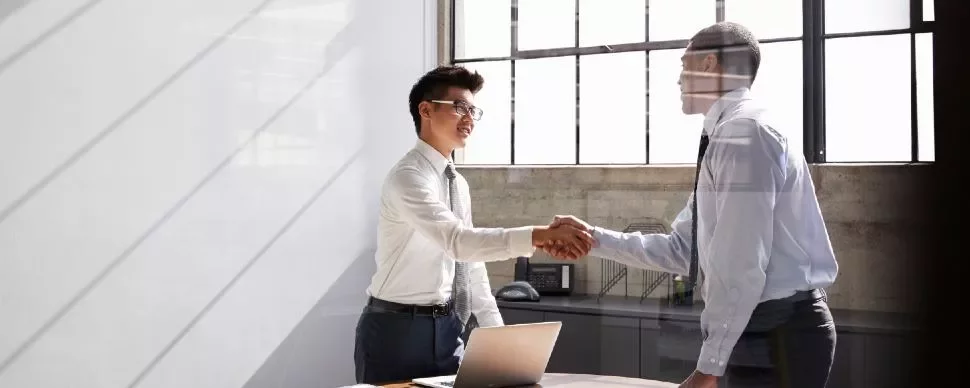 Two men shaking hands in an office setting.