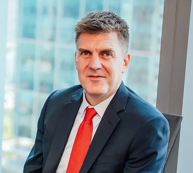 Man in a suit with a red tie sitting by a window with city view.