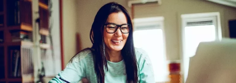 Smiling person with glasses using a laptop at home.