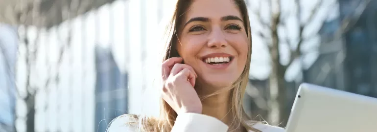 Woman smiling while using a phone outdoors.
